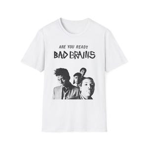 Op de afbeelding: Een wit t-shirt met korte mouwen en een zwart-witte grafische print van de band Bad Brains. De tekst ARE YOU READY staat boven de bandnaam BAD BRAINS in een verweerd zwart lettertype, gecentreerd op de borst van het kledingstuk.