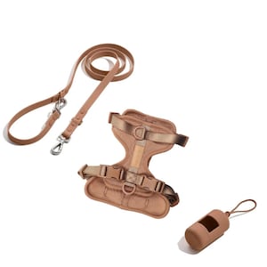 May include: A tan dog walking set comprising a lead, harness, and waste bag dispenser. The lead has a metal clasp and handle. The harness has adjustable straps and buckles. The waste bag dispenser is cylindrical with a loop.