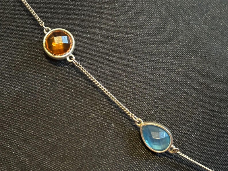 May include: A silver chain necklace with a round amber-colored gemstone and a teardrop-shaped blue gemstone.