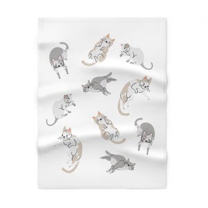 Puede incluir: Una manta rectangular blanca con un patrón repetitivo de gatos ilustrados en varias posturas. Los gatos están representados en tonos gris, blanco y marrón claro, mostrando diferentes posiciones de sueño, estiramiento y sentado sobre la tela.