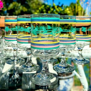 May include: A set of six clear glass goblets with colorful horizontal stripes in teal, yellow, pink, and blue. Each goblet features a teal bird design and a rounded base, perfect for serving beverages.