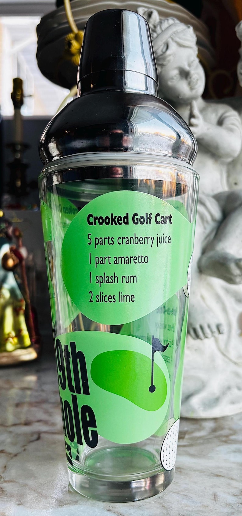 May include: A white ceramic mug with a black handle and the text "But First, Coffee" in a black, handwritten-style font. The mug is on a white surface.