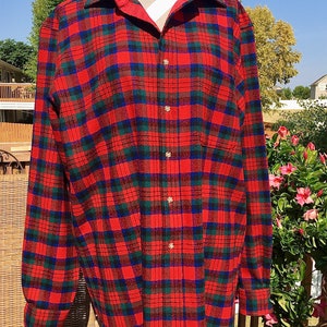 May include: A red, green, and blue plaid flannel shirt with a red collar. The long-sleeved shirt has gold-colored buttons and a single chest pocket. The shirt is displayed on a mannequin.