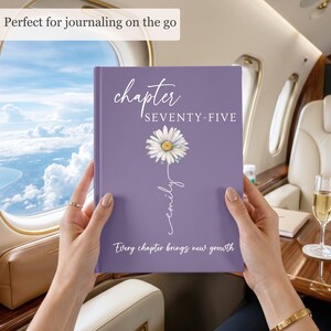 May include: A purple hardcover journal featuring the text "chapter SEVENTY-FIVE" at the top, a white daisy illustration with the name "emily" written in script as the stem, and the phrase "Every chapter brings new growth" at the bottom.