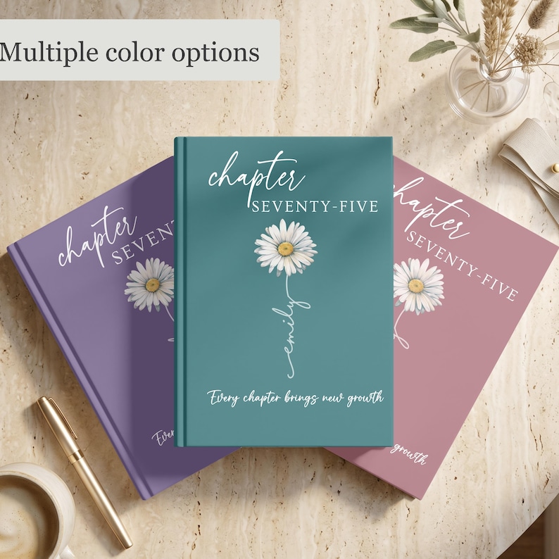 May include: Three hardcover books in teal, purple, and dusty rose colors. Each cover features a white daisy illustration, the text "chapter SEVENTY-FIVE", a name in script, and the phrase "Every chapter brings new growth" in white lettering.