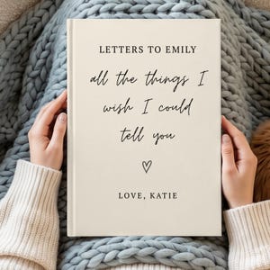 May include: A cream-colored hardcover book with black text that reads: LETTERS TO EMILY, all the things I wish I could tell you, a small heart icon, and LOVE, KATIE. The book cover has a clean, minimalist design with a mix of serif and script fonts.