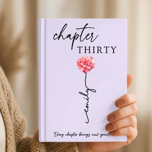 Może przedstawiać: Jasnofioletowy notatnik w twardej oprawie z czarnym napisem "chapter THIRTY" u g&oacute;ry, ilustracją r&oacute;żowego goździka z czarną łodygą w formie kursywy tworzącą imię "emily" oraz napisem "Every chapter brings new growth" na dole.