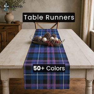 Könnte beinhalten: Ein blau-lila-schwarz karierter Tischläufer liegt auf einem weißen Holztisch. Der Text "Table Runners" und "50+ Colors" sind auf dem Bild zu sehen. Ein Metalltablett mit Tannenzapfen und dekorativen Kugeln liegt auf dem Läufer.