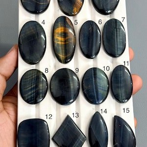Puede incluir: Un tablero de exhibición con quince piedras preciosas de ojo de halcón pulidas en varias formas, incluyendo óvalos, un diamante y una lágrima. Cada piedra está numerada del 1 al 15, con el código MG-022 impreso en la esquina inferior derecha.