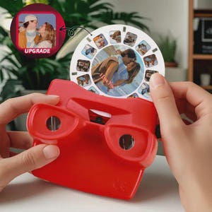 Op de afbeelding: Een rode View-Master-speelgoed met een ronde rol met meerdere afbeeldingen. De rol toont een stel dat elkaar omhelst, met de woorden "I Love You" erop gedrukt. Een kleine inset-afbeelding toont een stel met het woord "UPGRADE".