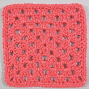 Può includere: Un pezzo quadrato all'uncinetto color corallo. L'articolo fatto a mano presenta un design aperto e traforato con un motivo ripetuto di fori quadrati. I bordi sono rifiniti con cura e il filato appare morbido e strutturato. Questo articolo potrebbe essere un sottobicchiere o parte di un progetto artigianale più ampio.