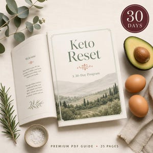 Op de afbeelding: Een open boek met de titel "Keto Reset" met een landschapsillustratie. De tekst op de omslag luidt "A 30-Day Program". Naast het boek liggen twee bruine eieren, een gehalveerde avocado en takjes rozemarijn en eucalyptus. De tekst "PREMIUM PDF GUIDE • 25 PAGES" staat onderaan.