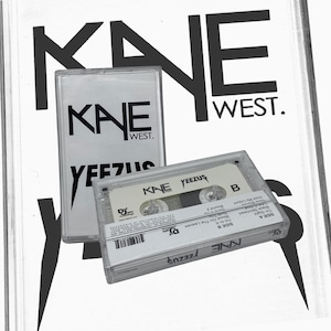 Op de afbeelding: Twee transparante cassettes met de tekst "KANE WEST" en "YEEZUS". De cassettes zitten in transparante plastic hoesjes. De achtergrond toont de woorden "KANE WEST" in grote, vette, zwarte letters.