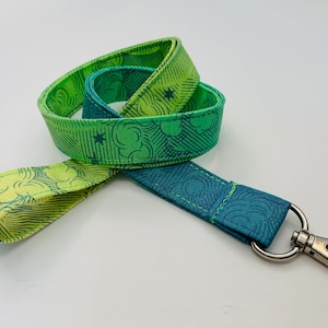 May include: A fabric lanyard with a swivel clasp. The lanyard features a repeating pattern of clouds and stars in shades of green and blue. The lanyard is approximately 36 inches long.