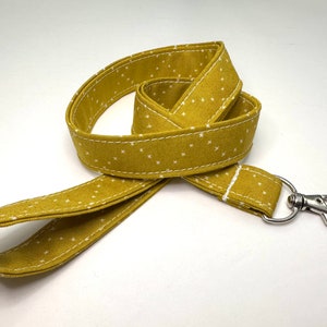 Può includere: Un laccio in tessuto giallo con pois bianchi e un moschettone girevole argentato.