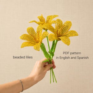 May include: A bouquet of three bright yellow beaded lilies with green beaded stems and leaves. The text on the left reads beaded lilies and the text on the right reads PDF pattern in English and Spanish, describing the craft project.