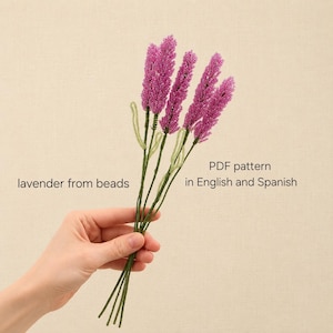 May include: A bouquet of four beaded lavender stems with vibrant purple flower heads and thin green wire stalks. The text on the image reads: lavender from beads, PDF pattern in English and Spanish. The stems are held together at the base.