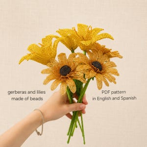May include: A bouquet of yellow beaded flowers including gerberas and lilies with dark centers. The text on the image reads: gerberas and lilies made of beads, PDF pattern in English and Spanish. The flowers have green stems and petals.