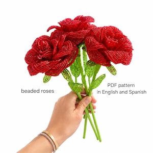 May include: A bouquet of three beaded roses in vibrant red, with green stems and leaves. The image includes the text "beaded roses" and "PDF pattern in English and Spanish". The roses are held against a white background.