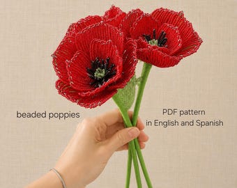 May include: Two handcrafted beaded poppies with vibrant red petals and dark centers, featuring green stems. The text on the image reads: beaded poppies, PDF pattern in English and Spanish. These decorative floral items are made from small beads.