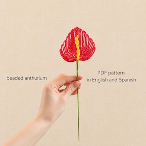 May include: A beaded anthurium flower crafted with red beads forming the spathe and yellow beads for the spadix, attached to a green stem. The text reads: beaded anthurium, PDF pattern in English and Spanish.