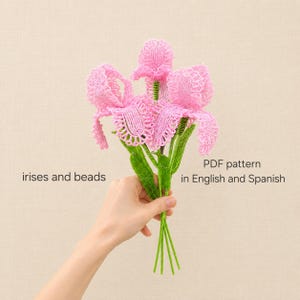 May include: A bouquet of three pink beaded iris flowers with green beaded stems and leaves. The text on the image reads: irises and beads, PDF pattern in English and Spanish. The flowers are constructed from small pink beads with green accents.