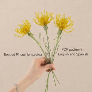 May include: Three beaded pincushion protea flowers with bright yellow petals and light green stems. The text on the image reads: Beaded Pincushion protea, PDF pattern in English and Spanish. The flowers are crafted from small beads.
