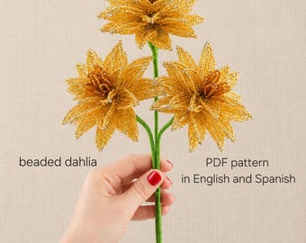 May include: Three golden yellow beaded dahlia flowers on green stems. The text on the image reads: beaded dahlia, PDF pattern in English and Spanish. The flowers are constructed from small, reflective beads arranged in a layered petal design.