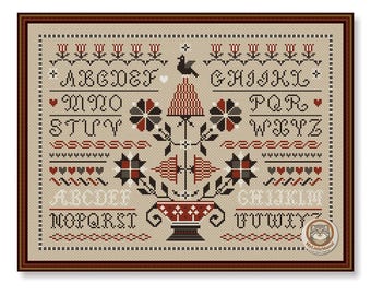 May include: Framed cross-stitch sampler with a beige background, featuring red, black, and white floral and geometric patterns. The design includes the alphabet, a bird, and a decorative vase. The frame is brown.