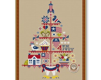 May include: A cross-stitch pattern on beige fabric featuring a tree-shaped arrangement of patriotic icons including a rocket, a bird, a cupcake, a house, and the text 4TH JULY in red, white, and blue, all framed in a simple brown wooden frame.
