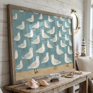 May include: A framed rectangular wall art print featuring a repeating pattern of white seagulls with yellow beaks on a light blue background, with a tan sandy strip along the bottom edge, housed in a weathered light brown wooden frame.