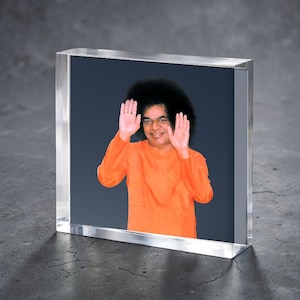 Puede incluir: Un bloque acrílico transparente con un retrato de un hombre con una prenda naranja con las manos levantadas. El fondo es de color azul oscuro. El bloque acrílico está sobre una superficie gris.