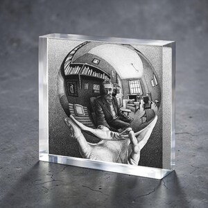 May include: A clear acrylic block featuring a black and white illustration of a man in a room held in a hand. The artwork is a detailed drawing with a surreal, Escher-like quality, showcasing a unique perspective and depth.