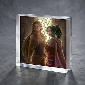 May include: A clear acrylic block featuring a fantasy art print of two women. One woman has long blonde hair and wears a gold-toned outfit. The other has green hair and a red and gold outfit. The artwork is set in a room with a window.