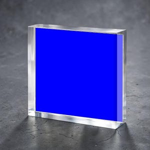 May include: A clear acrylic block with a vibrant blue insert. The block is rectangular and stands upright, showcasing the bold color against a neutral background. The edges of the block are polished, creating a clean and modern aesthetic.