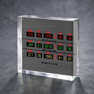 Puede incluir: Un bloque de acrílico transparente encierra una pantalla de tiempo con tres filas de lecturas digitales. La fila superior muestra "Destination Time" con la fecha y la hora. La fila del medio muestra "Present Time". La fila inferior muestra "Last Time Departed".