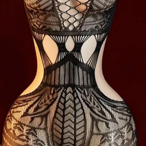 Puede incluir: Body de encaje negro con intrincados diseños calados. La prenda de una pieza presenta un diseño entrecruzado en el pecho y cortes en la cintura. El body se exhibe en un maniquí sobre un fondo rojo oscuro.