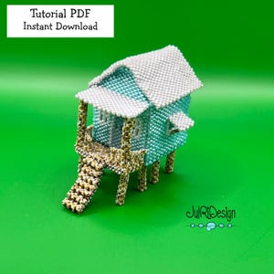 Op de afbeelding: Een miniatuur kralen huis met lichtblauwe muren, een wit dak en beige steunen. Het heeft een kleine veranda en een trap. De tekst "Tutorial PDF Instant Download" is zichtbaar. De achtergrond is heldergroen.