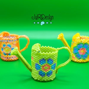 May include: Three miniature beaded watering cans in green, yellow, and orange with floral designs. The watering cans are made of small beads and have a flower design on the front.