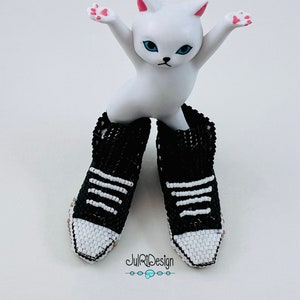 Peut inclure: Une figurine de chat blanc portant une paire de baskets en perles noires et blanches. Les baskets ont des rayures blanches et un bout blanc.