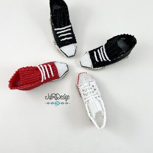 Peut inclure: Quatre mini-baskets en perles de couleur rouge, noire et blanche. Les baskets ont des lacets blancs et des bandes blanches sur les c&ocirc;t&eacute;s. Les baskets sont dispos&eacute;es en cercle sur un fond blanc.