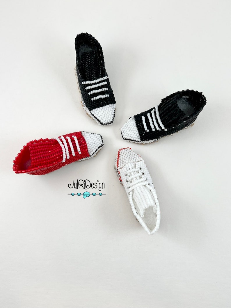 Peut inclure: Quatre mini-baskets en perles de couleur rouge, noire et blanche. Les baskets ont des lacets blancs et des bandes blanches sur les c&ocirc;t&eacute;s. Les baskets sont dispos&eacute;es en cercle sur un fond blanc.