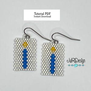 Può includere: Un paio di orecchini con perline bianche con un design a forma di candela blu e gialla. Gli orecchini sono attaccati a ganci d'argento. Il testo "JulRiDesign" è visibile nell'angolo in basso a destra dell'immagine.