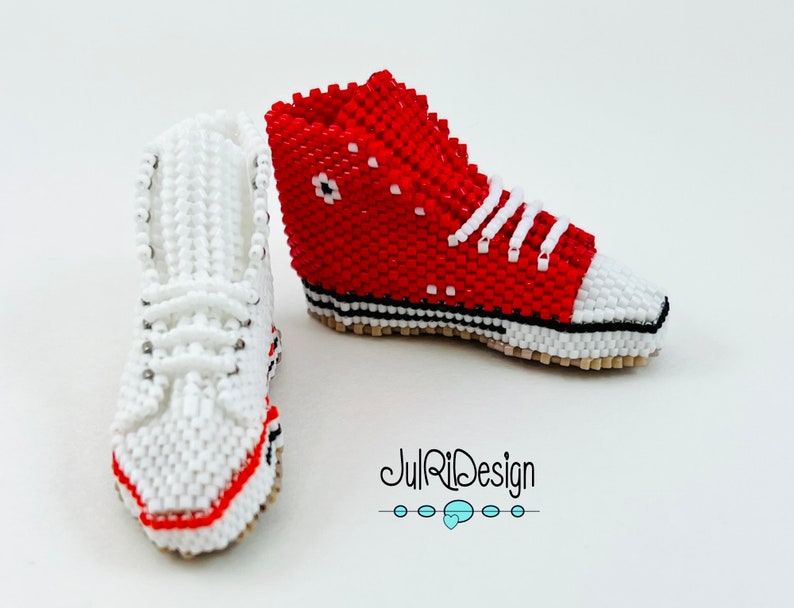 Peut inclure: Une paire de baskets miniatures en perles, une rouge et une blanche, avec des lacets blancs. Les baskets sont d&eacute;taill&eacute;es avec des coutures noires et une semelle blanche. L'image comprend le texte "JulRiDesign".