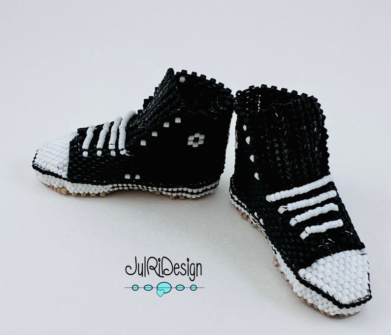 Peut inclure: Une paire de baskets en perles noires et blanches. Les baskets sont montantes et ont une semelle blanche. Les lacets sont blancs et les baskets ont un motif noir et blanc.