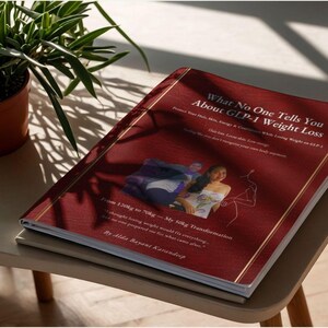 May include: A book titled "What No One Tells You About GLP-1 Weight Loss" with a burgundy cover and gold trim. The cover features text and images related to weight loss and transformation. The book is on a stack of other books.