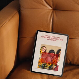 May include: A digital tablet displaying the text "YOUR TOOLS TO STAY CONSISTENT, SUPPORTED, AND IN CONTROL." The screen shows three women with sunflowers. The tablet is resting on a brown leather surface.