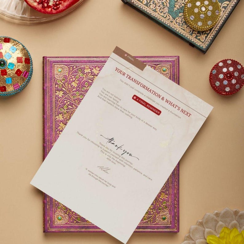 May include: A journal with a purple cover and gold floral design, with a card that reads "YOUR TRANSFORMATION & WHAT'S NEXT". The card also says "A FINAL REMINDER" and "thank you". Decorative boxes and a pomegranate half are also visible.