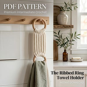 May include: A cream-colored, ribbed ring towel holder with wooden rings, holding a green towel. The text "PDF PATTERN" and "The Ribbed Ring Towel Holder" are visible. The towel holder is hanging on a white tiled wall.