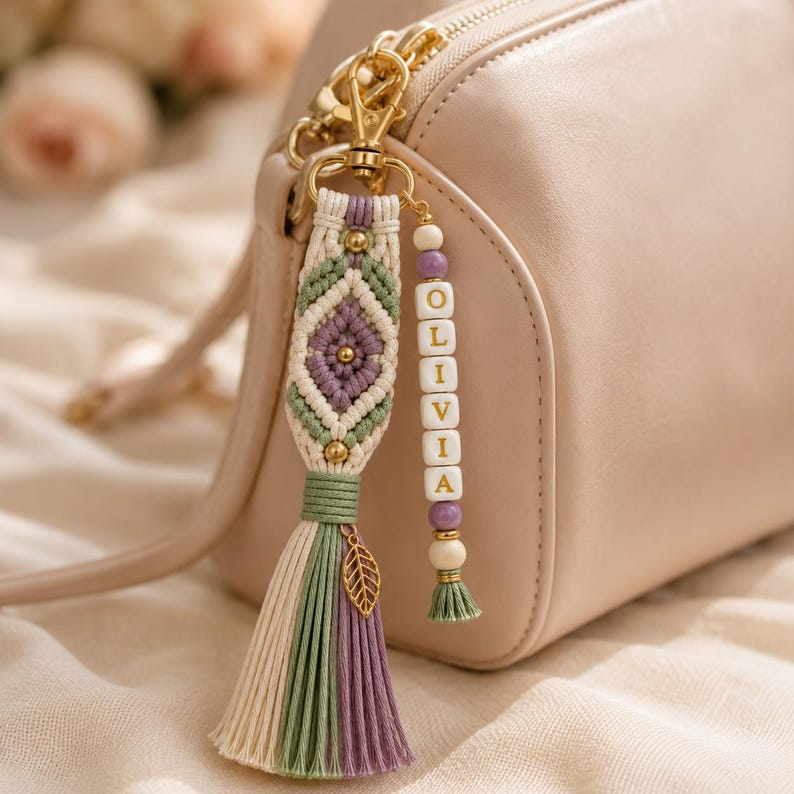 Puede incluir: Un colgante de macram&eacute; para bolso con patr&oacute;n de rombos en cord&oacute;n color crema, verde salvia y lavanda. Incluye un cierre de mosquet&oacute;n dorado, un peque&ntilde;o dije de hoja dorada y una hilera vertical de cuentas cuadradas blancas con el nombre OLIVIA.